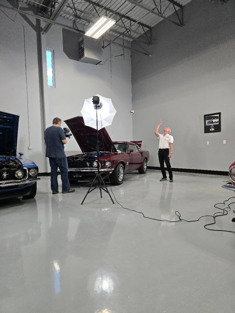 Jim Guthrie and a camera operator filming a burgundy Mustang in the garage